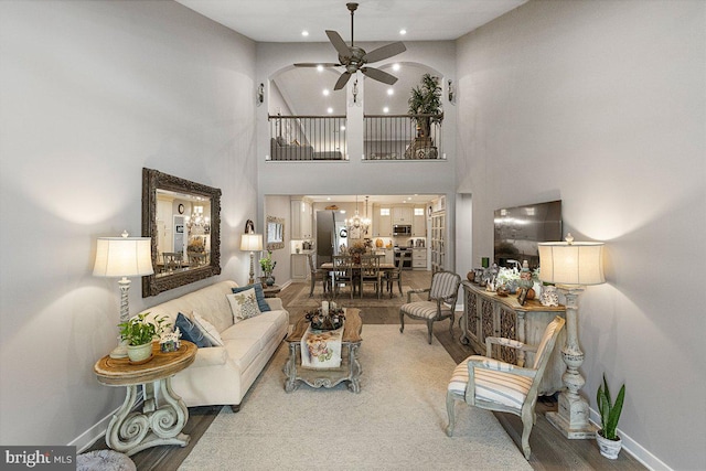 living room with ceiling fan with notable chandelier, a towering ceiling, and hardwood / wood-style floors