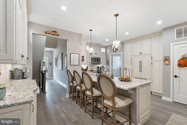 kitchen featuring light stone counters, hanging light fixtures, hardwood / wood-style flooring, appliances with stainless steel finishes, and a kitchen bar