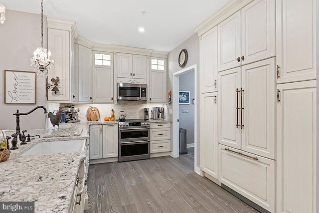 kitchen with light stone counters, hanging light fixtures, light hardwood / wood-style flooring, stainless steel appliances, and a notable chandelier