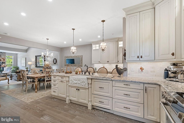 kitchen with high end stove, light stone countertops, pendant lighting, hardwood / wood-style flooring, and a notable chandelier