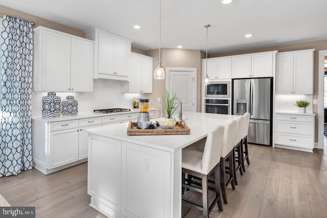 kitchen featuring white cabinets, a center island with sink, stainless steel appliances, and pendant lighting