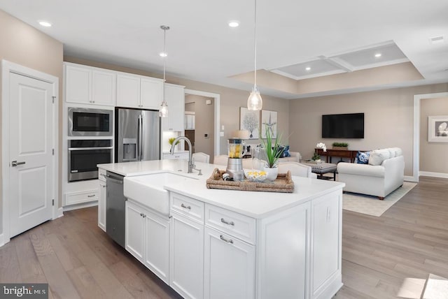 kitchen with white cabinets, pendant lighting, a center island with sink, stainless steel appliances, and light hardwood / wood-style floors