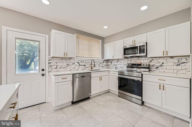 kitchen featuring appliances with stainless steel finishes, decorative backsplash, white cabinets, light stone countertops, and sink