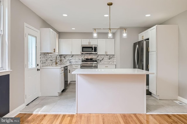 kitchen with pendant lighting, appliances with stainless steel finishes, light wood-type flooring, and a kitchen island