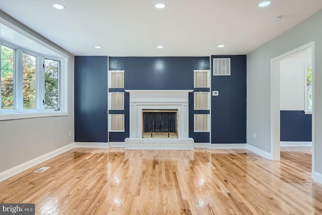 unfurnished living room featuring light hardwood / wood-style flooring and a brick fireplace