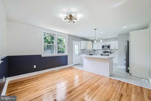 kitchen with appliances with stainless steel finishes, white cabinetry, pendant lighting, a center island, and light hardwood / wood-style flooring