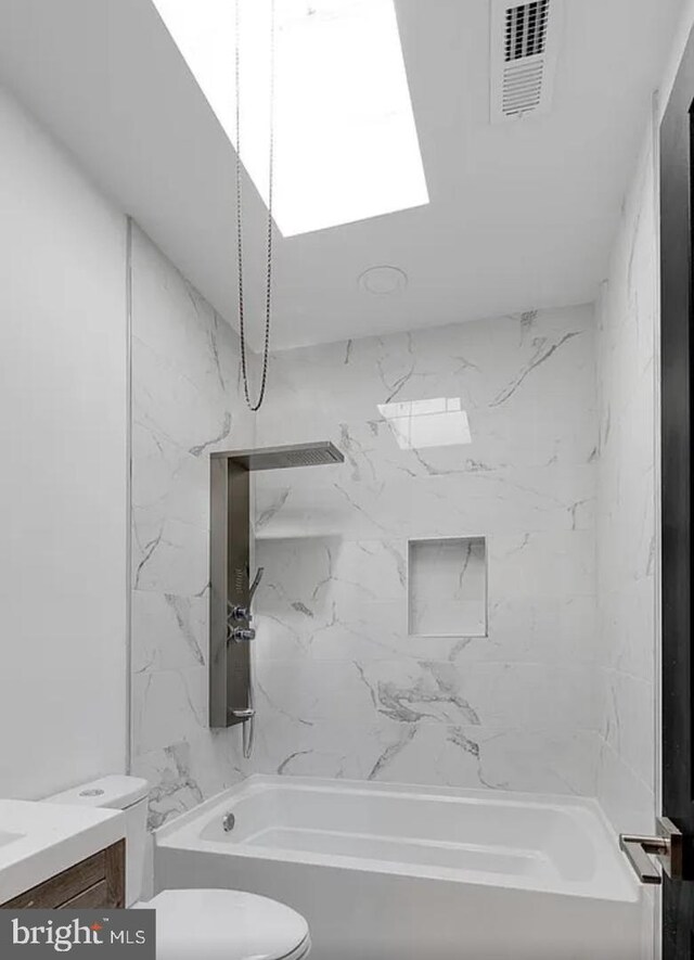 full bathroom with a skylight, vanity, toilet, and tiled shower / bath combo