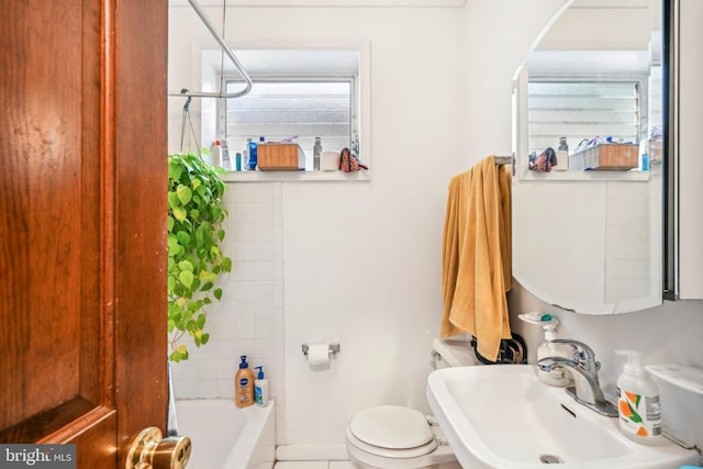 full bathroom with tiled shower / bath, toilet, sink, and a wealth of natural light