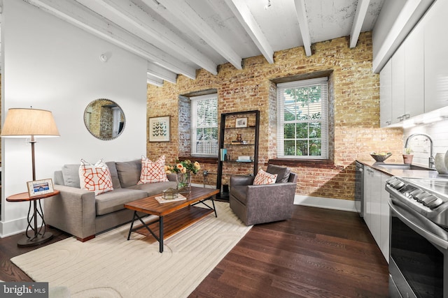 living room featuring beam ceiling, sink, dark wood-type flooring, and brick wall