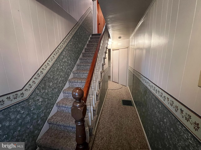 stairs with wooden walls, ornamental molding, and carpet