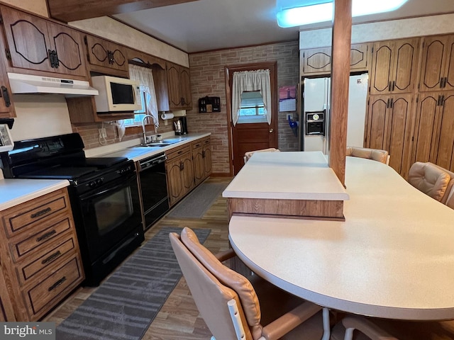 kitchen featuring wood-type flooring, a breakfast bar area, sink, black appliances, and brick wall