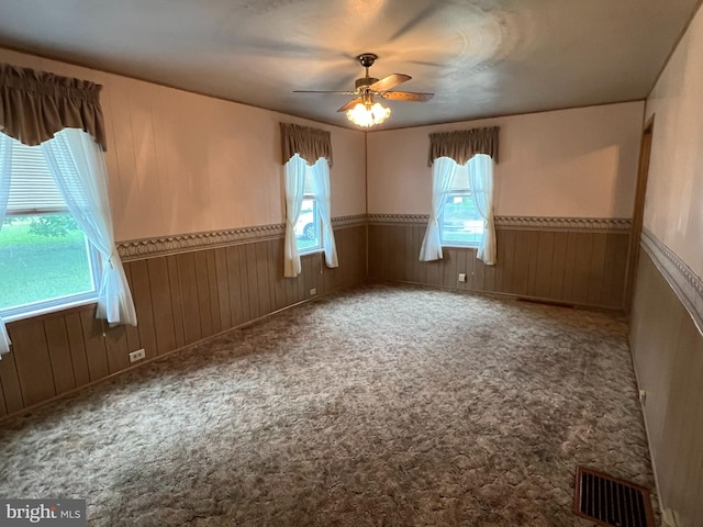 carpeted empty room with ceiling fan, wood walls, and a healthy amount of sunlight