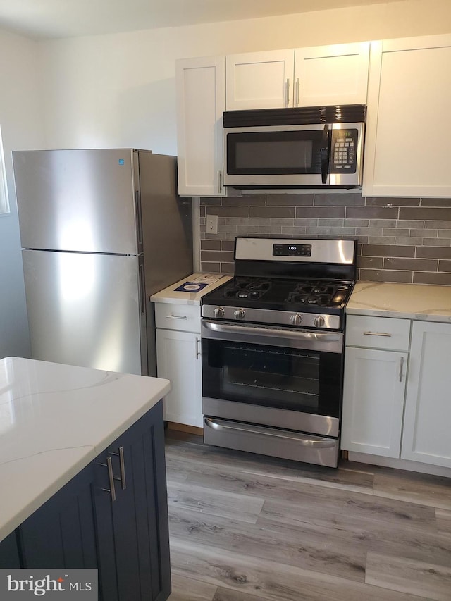 kitchen featuring stainless steel appliances, white cabinetry, light stone counters, and light wood-type flooring