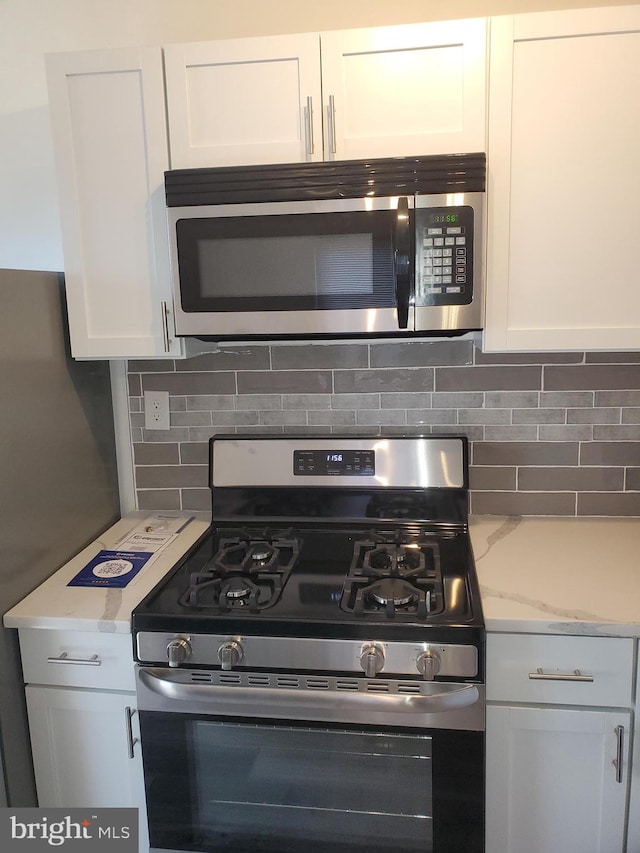 kitchen with decorative backsplash, white cabinetry, appliances with stainless steel finishes, and light stone countertops