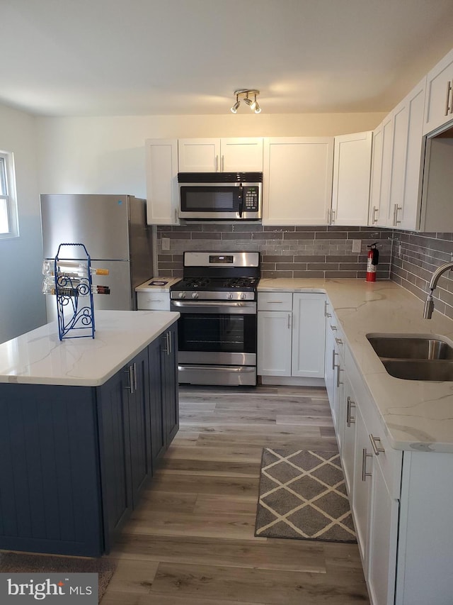 kitchen featuring light wood-type flooring, sink, white cabinets, appliances with stainless steel finishes, and light stone countertops