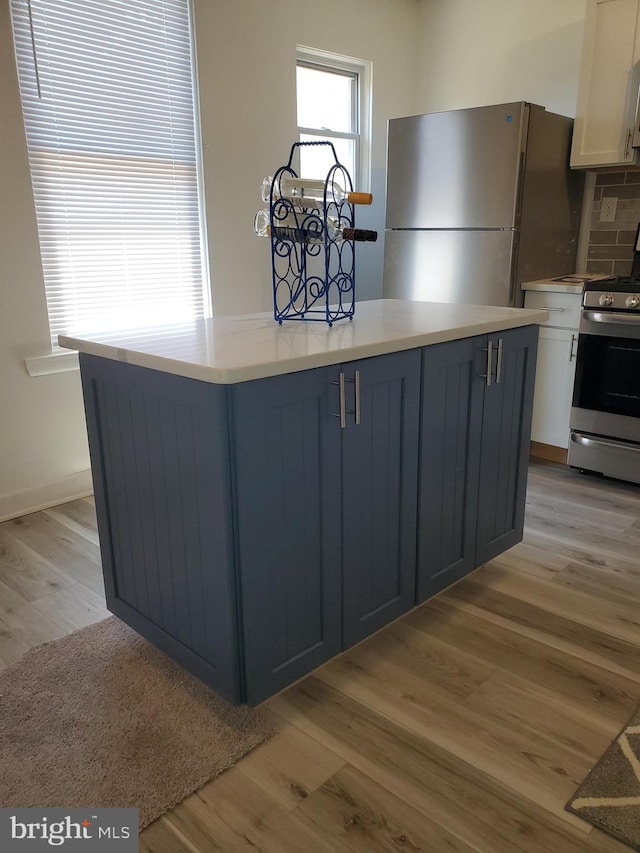 kitchen featuring blue cabinets, tasteful backsplash, white cabinetry, stainless steel appliances, and light hardwood / wood-style floors