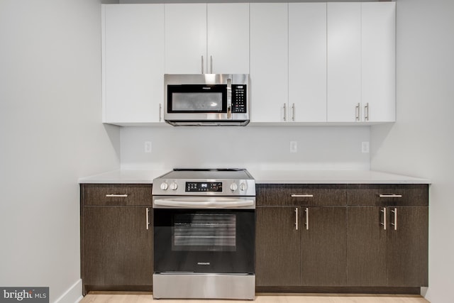 kitchen featuring appliances with stainless steel finishes, white cabinetry, dark brown cabinets, and light hardwood / wood-style flooring