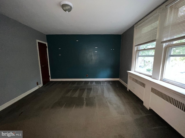 spare room featuring radiator and dark carpet