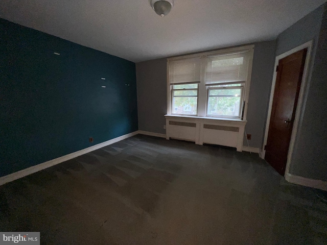 spare room featuring a textured ceiling, dark carpet, and radiator heating unit