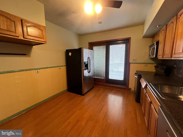 kitchen featuring tile walls, light hardwood / wood-style floors, sink, stainless steel appliances, and ceiling fan