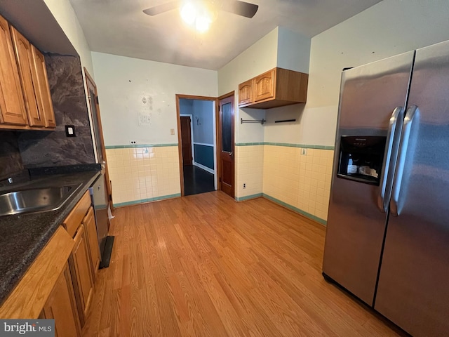 kitchen featuring ceiling fan, stainless steel refrigerator with ice dispenser, light wood-type flooring, and tile walls