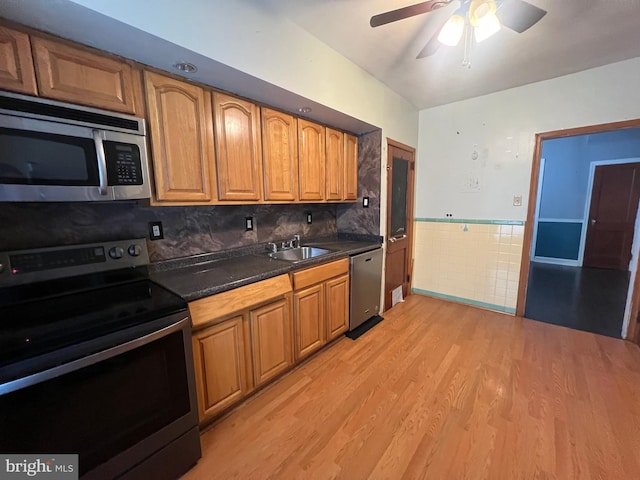 kitchen with ceiling fan, sink, light hardwood / wood-style flooring, stainless steel appliances, and dark stone counters