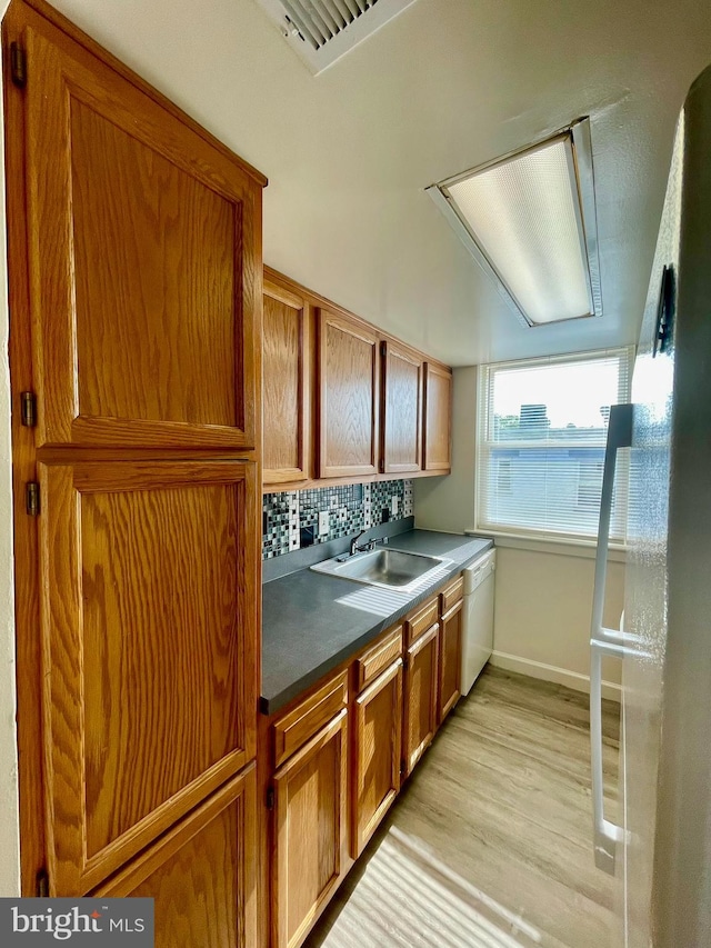 kitchen featuring backsplash, white dishwasher, light hardwood / wood-style floors, and sink