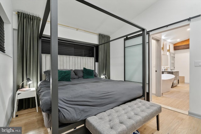 bedroom featuring connected bathroom, light hardwood / wood-style floors, vaulted ceiling, and a barn door