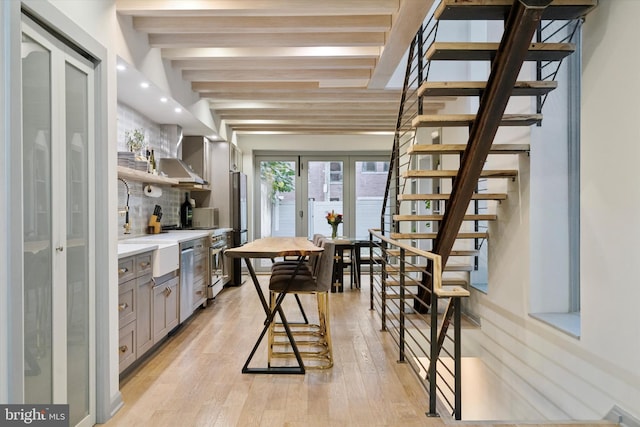 kitchen with light hardwood / wood-style floors, beamed ceiling, appliances with stainless steel finishes, and backsplash