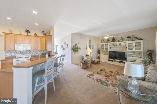 kitchen with ceiling fan, backsplash, white appliances, light brown cabinetry, and light colored carpet