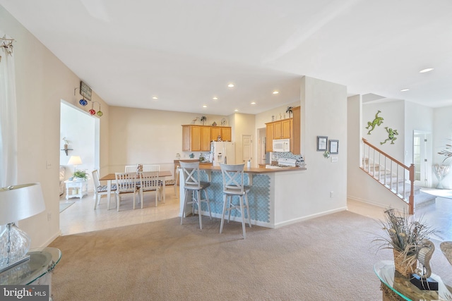 kitchen featuring white appliances, light colored carpet, kitchen peninsula, and a kitchen breakfast bar