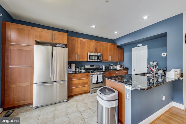 kitchen featuring kitchen peninsula, appliances with stainless steel finishes, dark stone counters, sink, and light tile patterned floors