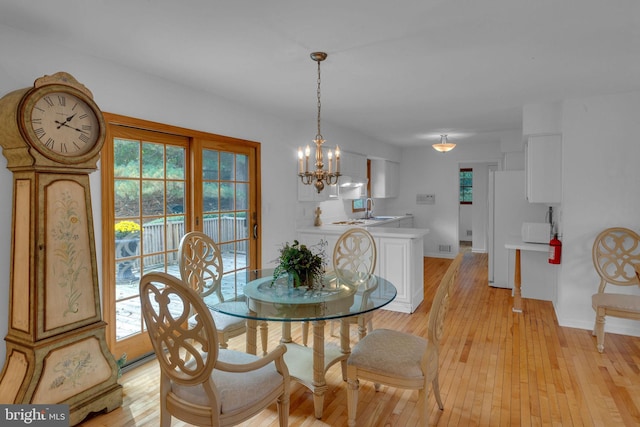 dining space with light wood-type flooring, an inviting chandelier, and sink