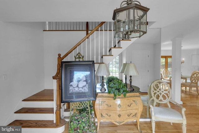 stairs featuring a notable chandelier, hardwood / wood-style flooring, decorative columns, and a wealth of natural light