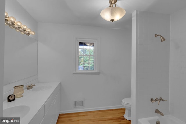 full bathroom featuring wood-type flooring, tiled shower / bath, vanity, and toilet