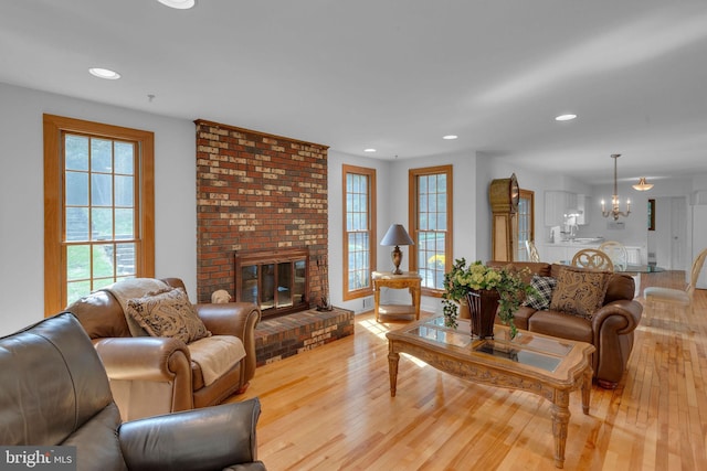 living room featuring light hardwood / wood-style floors, a chandelier, and a brick fireplace