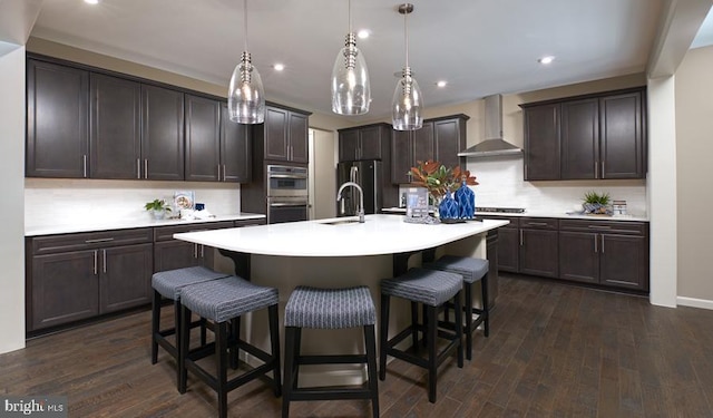 kitchen with decorative light fixtures, dark hardwood / wood-style flooring, wall chimney range hood, and an island with sink