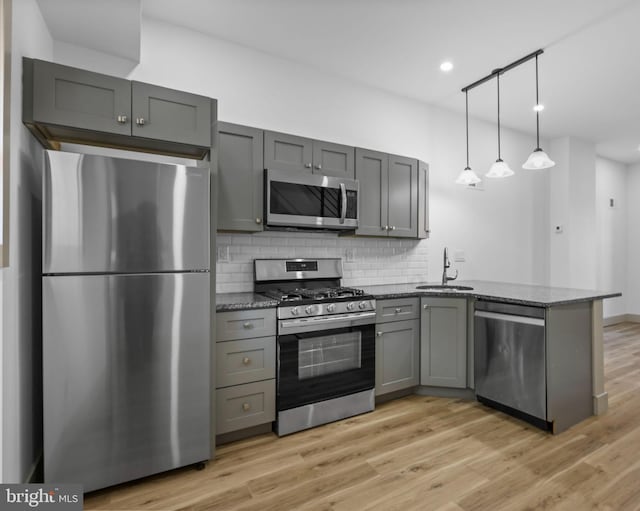 kitchen with kitchen peninsula, stainless steel appliances, dark stone countertops, gray cabinets, and light hardwood / wood-style floors