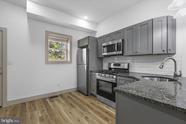 kitchen with dark stone countertops, sink, light wood-type flooring, gray cabinets, and appliances with stainless steel finishes