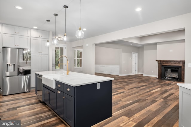 kitchen with appliances with stainless steel finishes, a center island with sink, sink, and dark hardwood / wood-style flooring