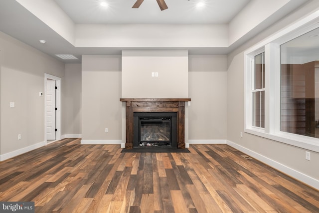 unfurnished living room featuring ceiling fan, a raised ceiling, and dark hardwood / wood-style floors