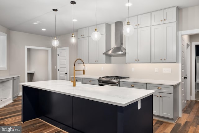 kitchen featuring a center island with sink, wall chimney range hood, stainless steel gas range oven, dark hardwood / wood-style floors, and light stone countertops