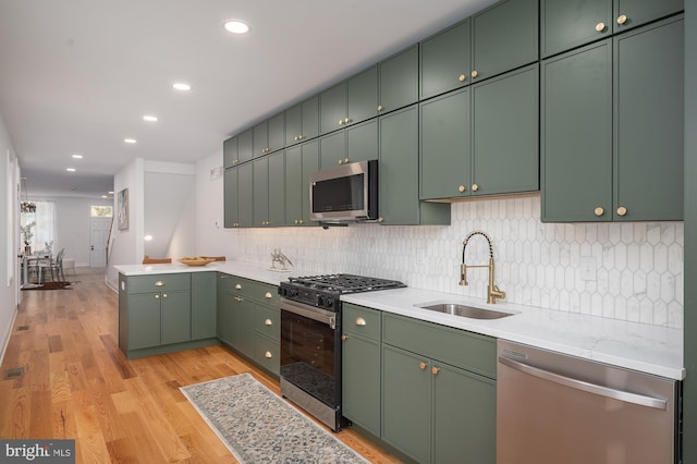 kitchen featuring tasteful backsplash, appliances with stainless steel finishes, sink, green cabinets, and light hardwood / wood-style floors