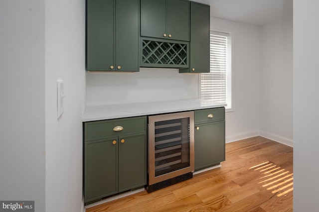 bar featuring wine cooler, green cabinets, and light wood-type flooring