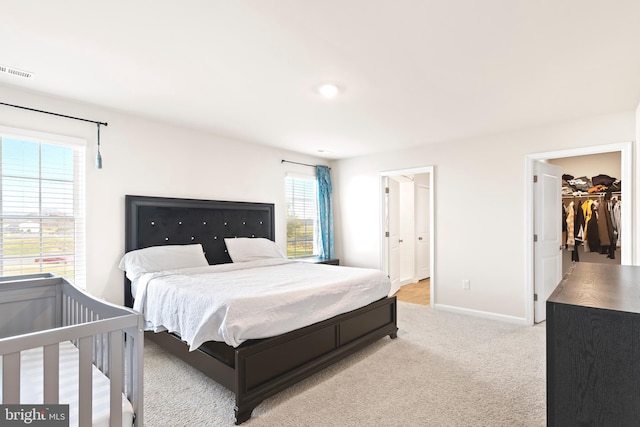 bedroom with connected bathroom, multiple windows, a spacious closet, and light colored carpet