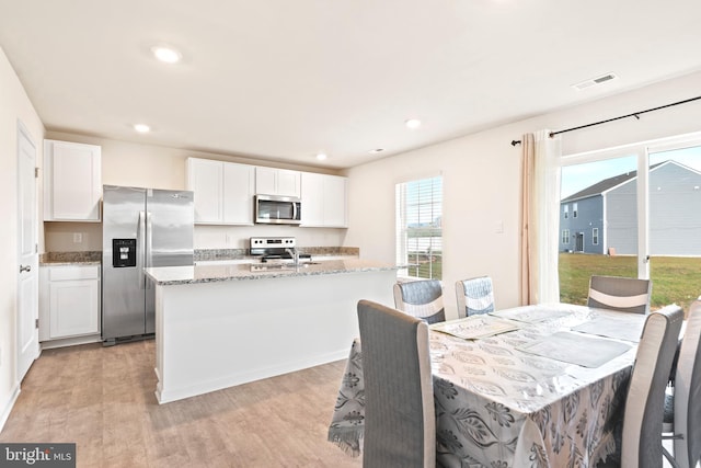 kitchen featuring white cabinetry, light stone counters, appliances with stainless steel finishes, a kitchen island with sink, and light hardwood / wood-style flooring