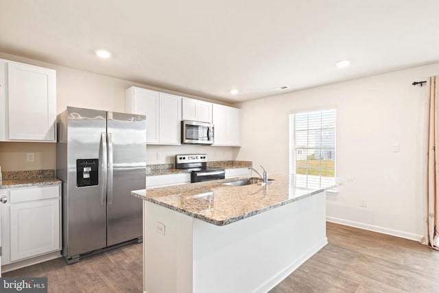 kitchen with stainless steel appliances, sink, a kitchen island with sink, white cabinetry, and light wood-type flooring