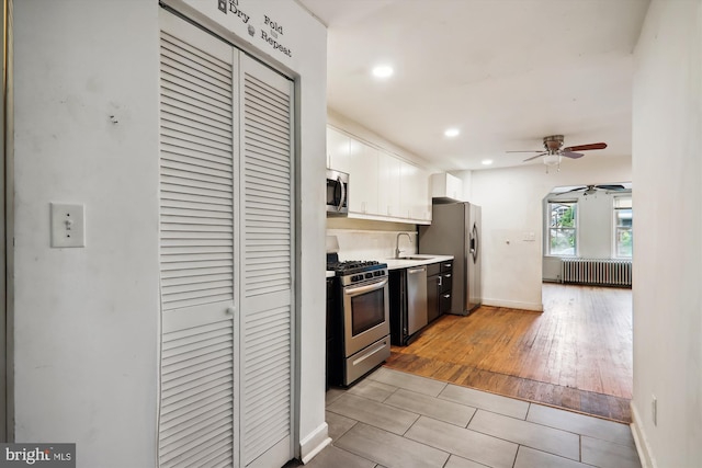 kitchen featuring light hardwood / wood-style floors, white cabinetry, stainless steel appliances, radiator, and ceiling fan