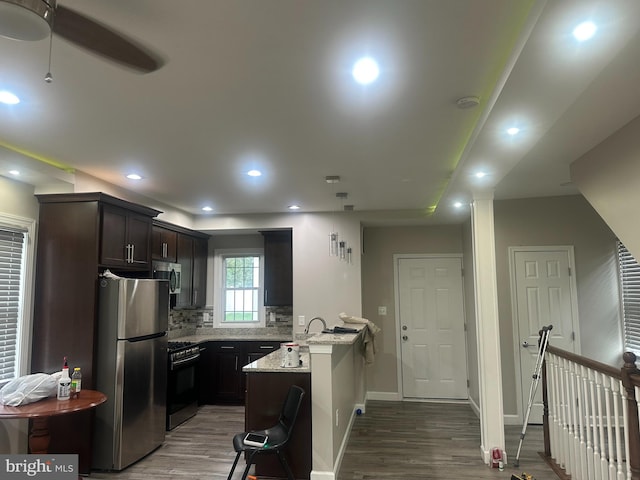 kitchen with light stone counters, appliances with stainless steel finishes, wood-type flooring, and a breakfast bar