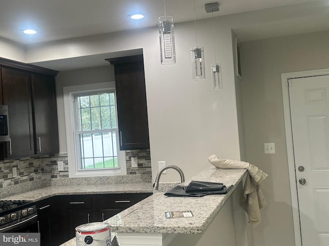 kitchen featuring light stone counters, stove, kitchen peninsula, sink, and backsplash